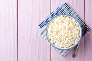 Cottage cheese in blue bowl on purple wooden background