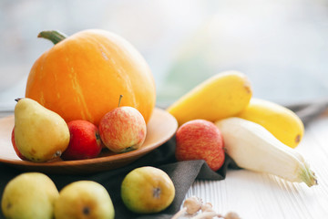 Pumpkin and zucchini in stylish wooden plate with apples and pears on linen apron on white wooden table in light.  Hello autumn concept and Fall Harvest. Happy Thanksgiving