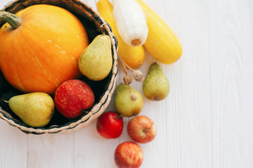 Hello autumn concept and Fall Harvest. Flat lay.  Pumpkin and zucchini in stylish straw basket with apples and pears on white wooden background in light, Space for text