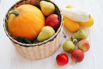 Hello autumn concept and Fall Harvest. Pumpkin and zucchini in stylish straw basket with apples and pears on white wooden background in light, Space for text. Happy Thanksgiving