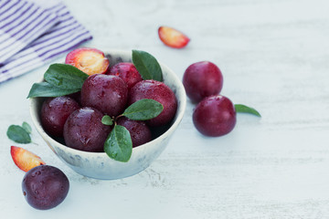 Fresh plums with leaves on rustic wooden table background.
