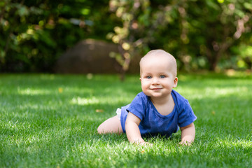 Cute little blond baby boy crawling on fresh green grass. Kid having fun making first steps on mowed natural lawn. Happy and healthy childhood concept