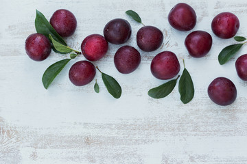 Fresh plums with leaves on white rustic wooden table background.