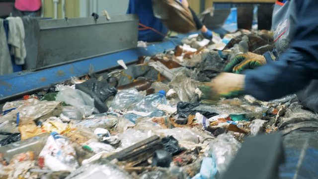 Two workers sort garbage moving on a conveyor at a recycling plant.