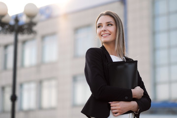 Young beautiful girl in the street next to the building in a jacket and with a notebook.
