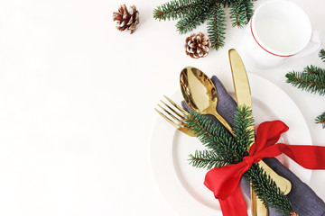 Traditional Christmas table place setting. Golden cutlery, linen napkin, spruce branches and cup of milk. Pine cone and red ribbon decoration. Holidays background. Flat lay, top view with copy space.