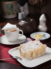A piece of cake Napoleon with a cup of tea in a restaurant on a red tablecloth