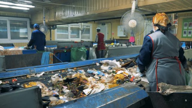 Garbage moves on conveyors, while workers sorting it at a recycling plant.