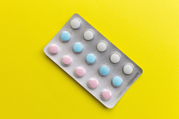 Colorful pills of white, blue and pink color in blister on yellow plain background.