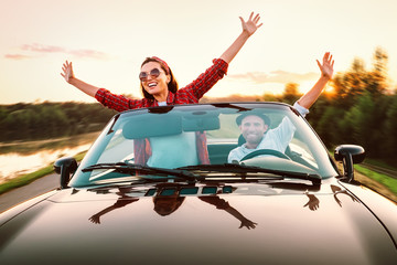 Traveling by car - happy couple in love go by cabriolet car in sunset time