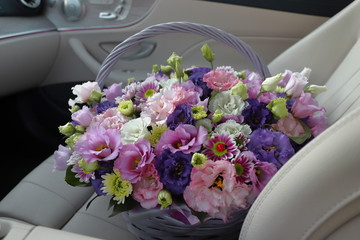 Wicker basket with lilac flowers on the leather seat of a luxury car