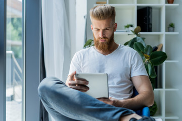 Multitasking. Handsome young man wearing glasses and working with touchpad while sitting on the couch in office