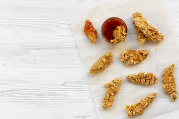 Overhead view, fried chicken strips with sauce on white wooden surface. Flat lay, from above, top view. Copy space and text area.