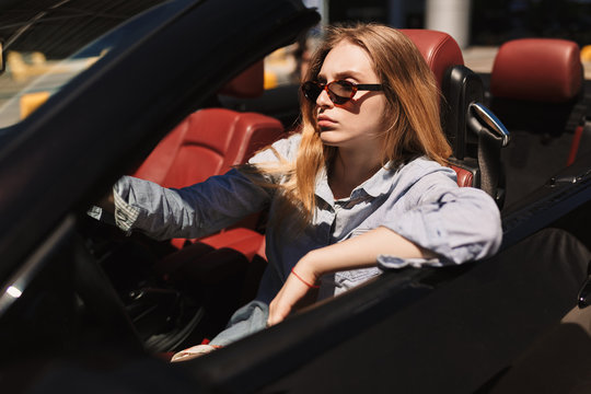 Young serious lady in sunglasses thoughtfully driving cabriolet car