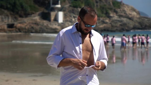 Young man undressing shirt on beautiful beach, super slow motion
