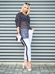 Full length young beautiful excited woman with gorgeous natural lips, blue and brown eyes in black blouse having fun with disposable white cup on urban metal strips background