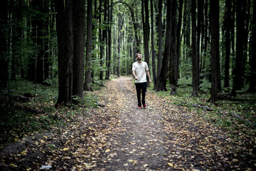 lonely young male hipster in casual walks in the autumn dark moody forest with fallen leaves