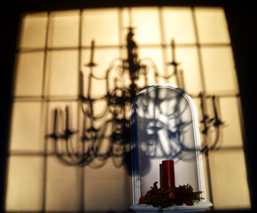 A shadow of a 3 tier chandelier on a wall with a niche and candle. 