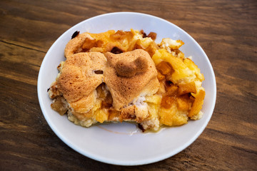 Casserole with apples, cheese and cottage cheese on a white porcelain plate on a wooden background.