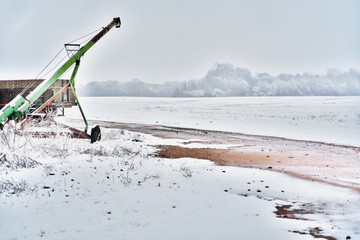 An old grain auger in a snowy field on an overcast day.