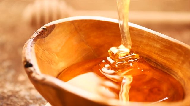 Honey dripping from honey dipper in wooden bowl. Healthy organic thick honey closeup. Slow motion. 3840X2160 4K UHD video footage