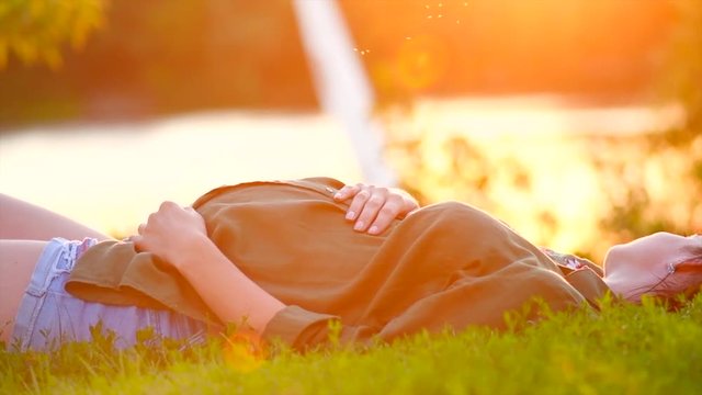 Healthy pregnancy concept. Pregnant woman touching her belly, lying on green grass in summer park. Slow motion. 3840X2160 4K UHD video footage