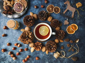 Cozy autumn morning with cup of tea with lemon, decorative corns, dried oranges, nuts and wooden toys on dark blue background, teatime, hugge concept, selective focus, top view