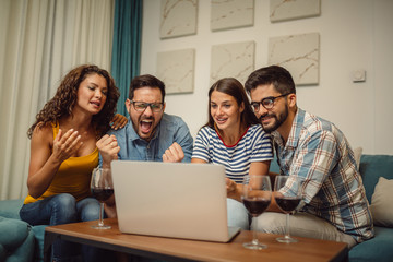 Young football fans are drinking beer,cheering and smiling while watching football game online on laptop.