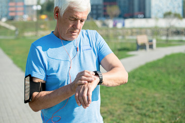 Waist up portrait of modern senior man setting up smart watch and listening to music while doing...