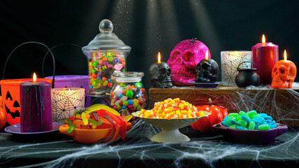 Happy Halloween trick or treat party table with bowls and apothecary jars of candy with skull...