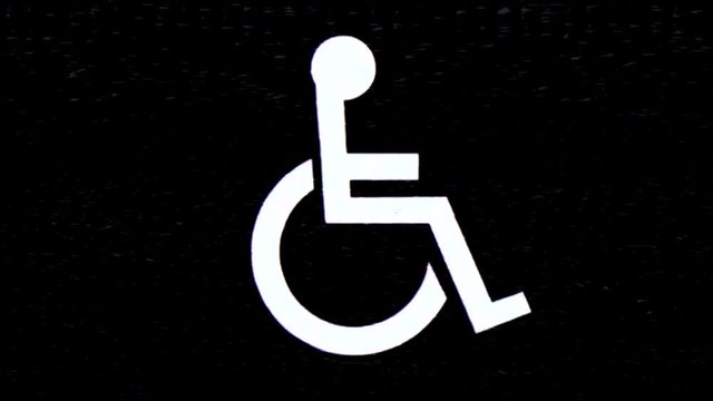 The stylized image of a person in a wheelchair (a symbol of access for disabled people), appearing with a heavy analog VHS distortion effect.
