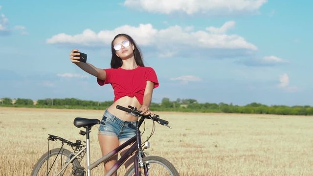 The girl makes selfie. A sporty girl with a bicycle takes a picture of herself on the phone.