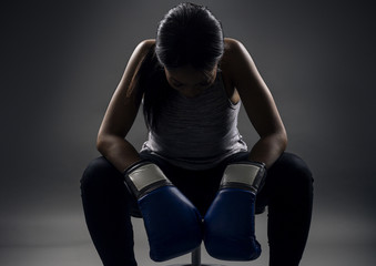 Black female wearing boxing gloves looking angry as a boxer, MMA fighter or self defense trainer sitting after working out. She is portraying female strength and determination.