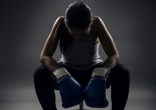 Black female wearing boxing gloves looking angry as a boxer, MMA fighter or self defense trainer sitting after working out.  She is portraying female strength and determination.