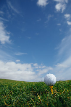 Golf Ball On Tee, Green Grass And Blue Sky Background