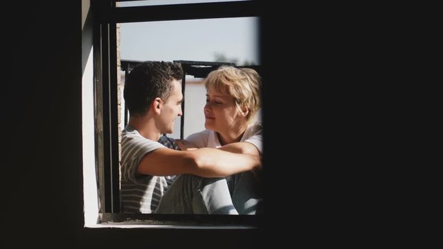 Happy multiethnic man and woman sitting together at beautiful sunny balcony, looking at each other, talking about life.