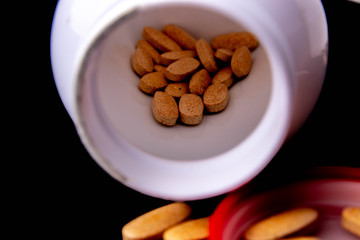 oval brown tablets inside a white bottle on a dark blue background