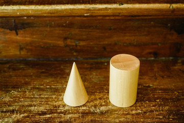 Solid wood shapes to study geometry and volumes, cones, triangles, squares, spheres on a warm wood background.