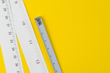 White measuring tapes with centimetre and inches on vivid yellow background with copy space, length, long or maker concept