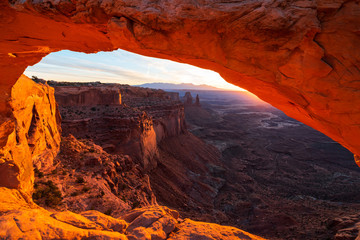 Cliff's-edge sandstone Mesa Arch framing an iconic sunrise view of the red rock canyon landscape...