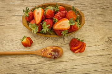 wooden bowl with strawberries and dulce de letche in spoon at wooden background