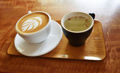 Latte Coffee with  tree shape on foam milk in white cup with hot tea in black  cup and flowerpot on wooden table 
