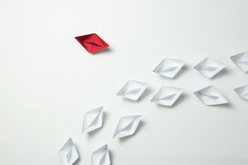 Red paper ship changing direction and white ones. New idea, change, trend, courage, creative...