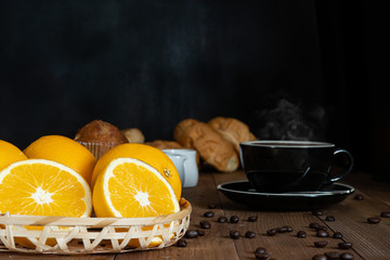 Breakfast set of hot coffee with croissant, banana cake and fresh orange fruits on wooden table with dark background
