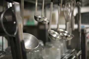 Ladles Hanging from a Stainless Steel Silver Metal Rack in an Industrial Kitchen
