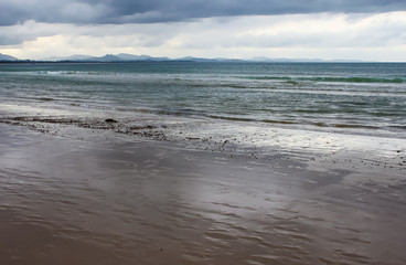 Wet beach as the tide recedes with blue mountains ranges in the distance under a stormy sky - Byron Bay NSW Australia