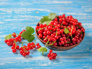 Freshly picked redcurrant berries in a clay bowl on a blue table. Natural food.