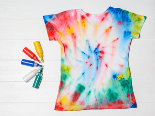 T-shirt painted in tie dye style with colors on a white wooden table. Flat lay.