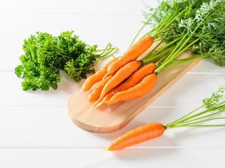 A bunch of carrots and a bunch of parsley on a cutting Board on a white table.