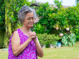 Elderly woman standing and pray in the garden.